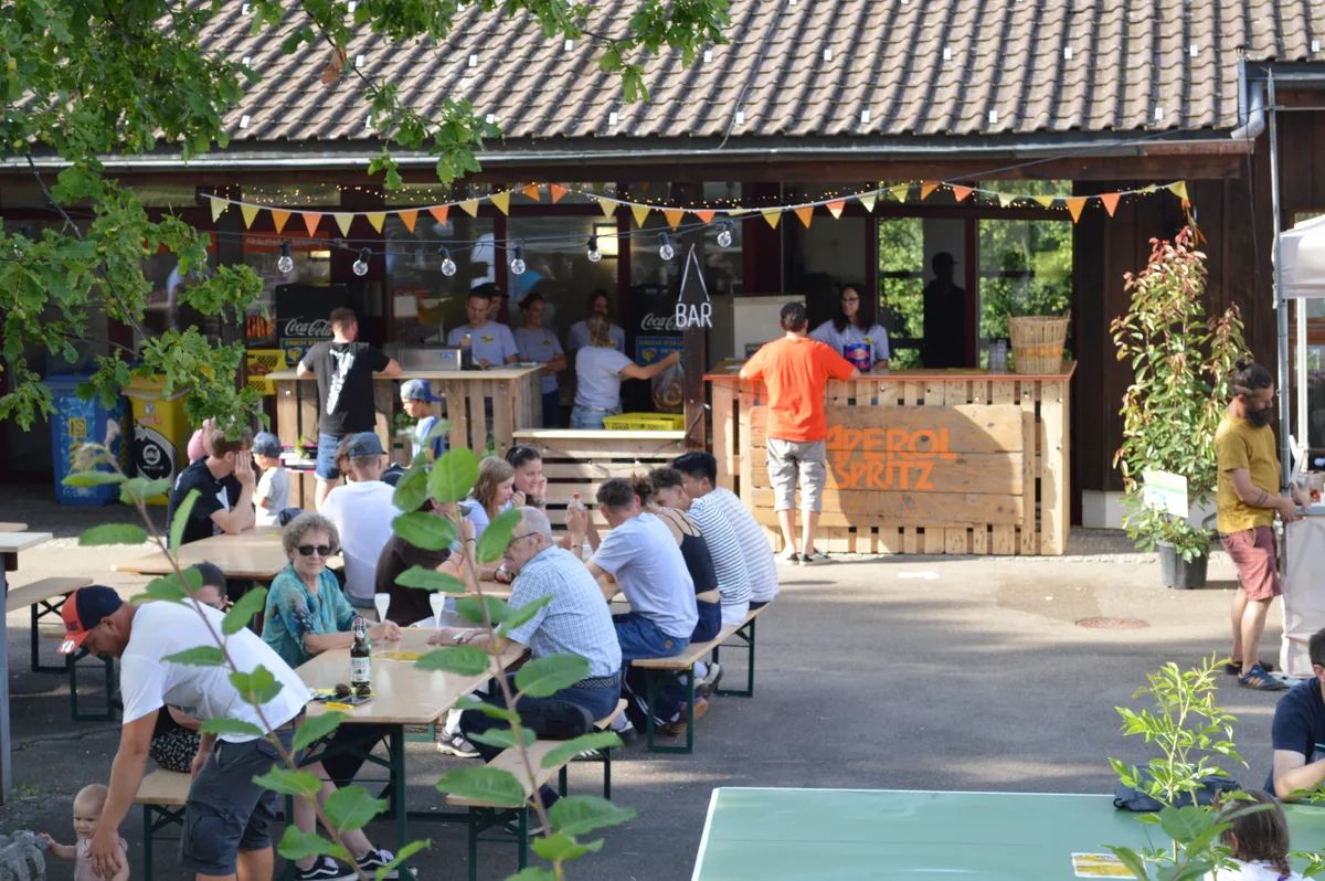 Ein Aussenplatz mit einer Bar und sitzenden Gästen.